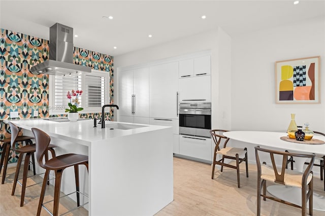 kitchen with light wood-type flooring, stainless steel oven, exhaust hood, sink, and white cabinets