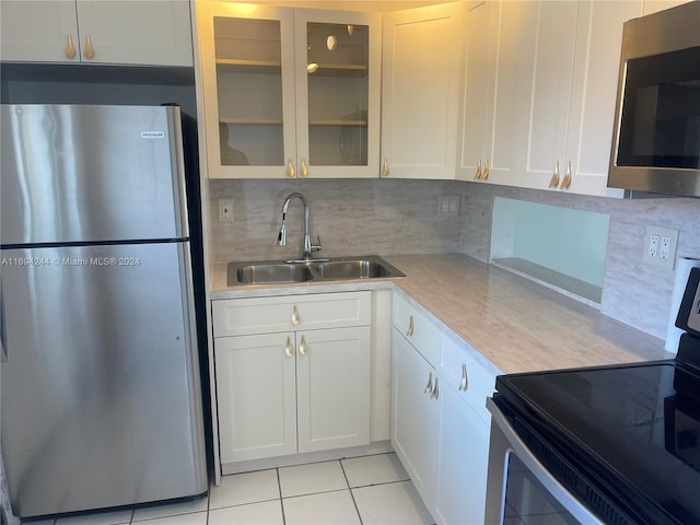 kitchen featuring sink, light tile patterned floors, decorative backsplash, white cabinets, and appliances with stainless steel finishes