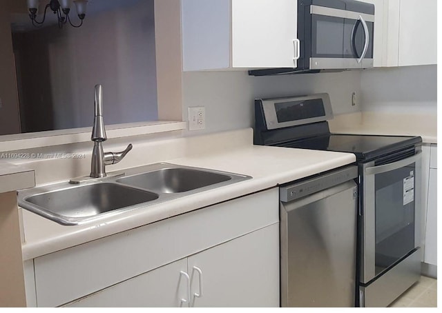 kitchen with white cabinets, sink, stainless steel appliances, and an inviting chandelier