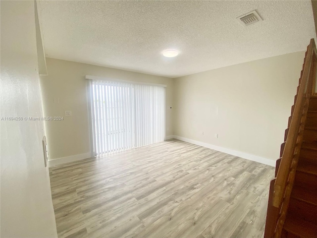 unfurnished room featuring a textured ceiling and light hardwood / wood-style flooring