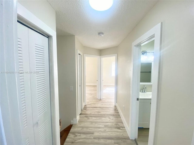 hall with sink, light hardwood / wood-style floors, and a textured ceiling