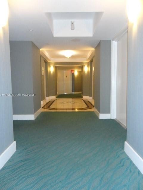 corridor featuring a raised ceiling and dark colored carpet