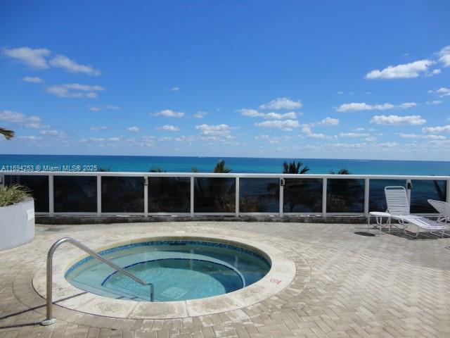 view of swimming pool featuring a patio, a hot tub, and a water view