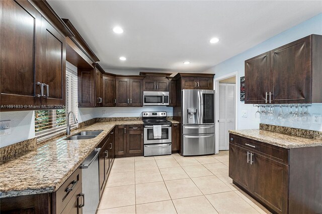 kitchen featuring appliances with stainless steel finishes, light stone counters, dark brown cabinets, and sink