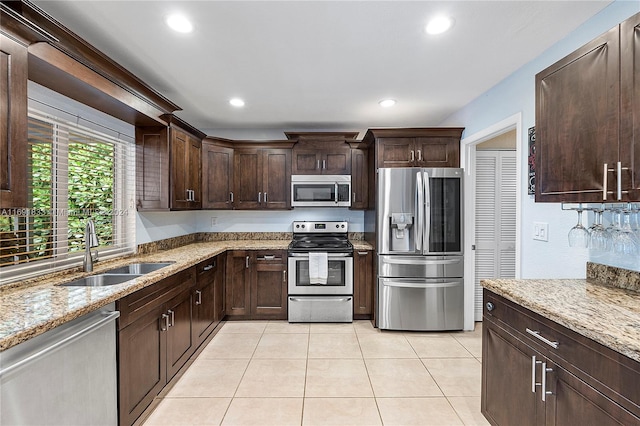 kitchen with sink, light tile patterned floors, light stone countertops, appliances with stainless steel finishes, and dark brown cabinetry