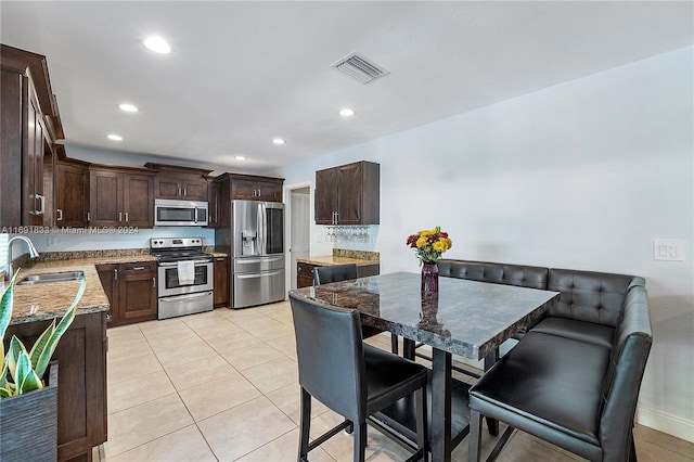 kitchen featuring dark brown cabinetry, sink, light tile patterned flooring, and appliances with stainless steel finishes