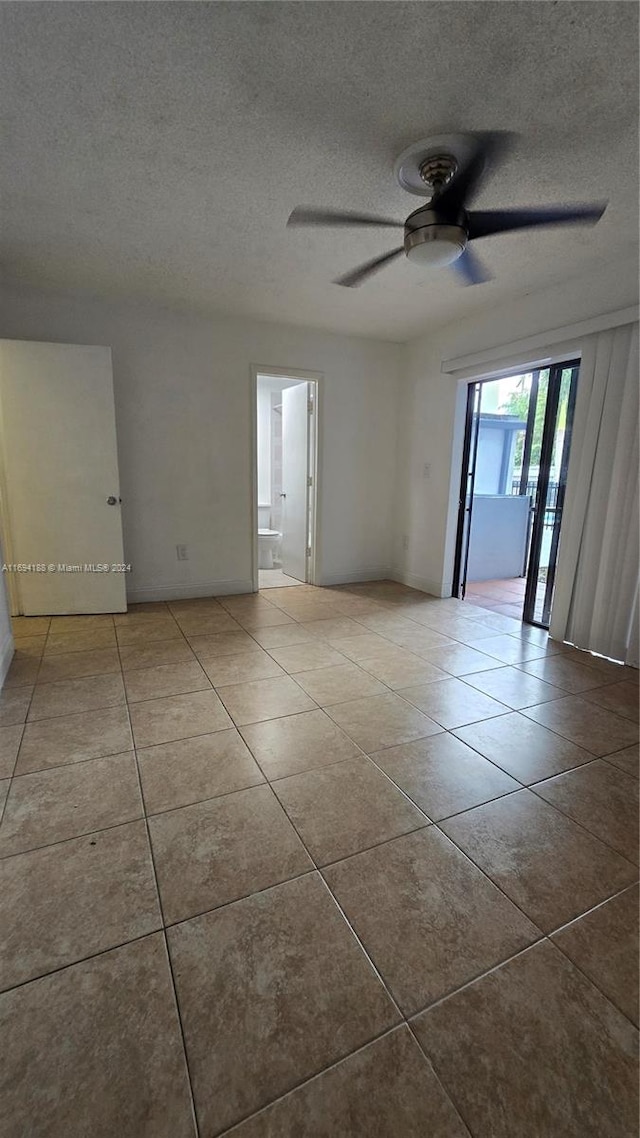 empty room featuring ceiling fan, light tile patterned floors, and a textured ceiling