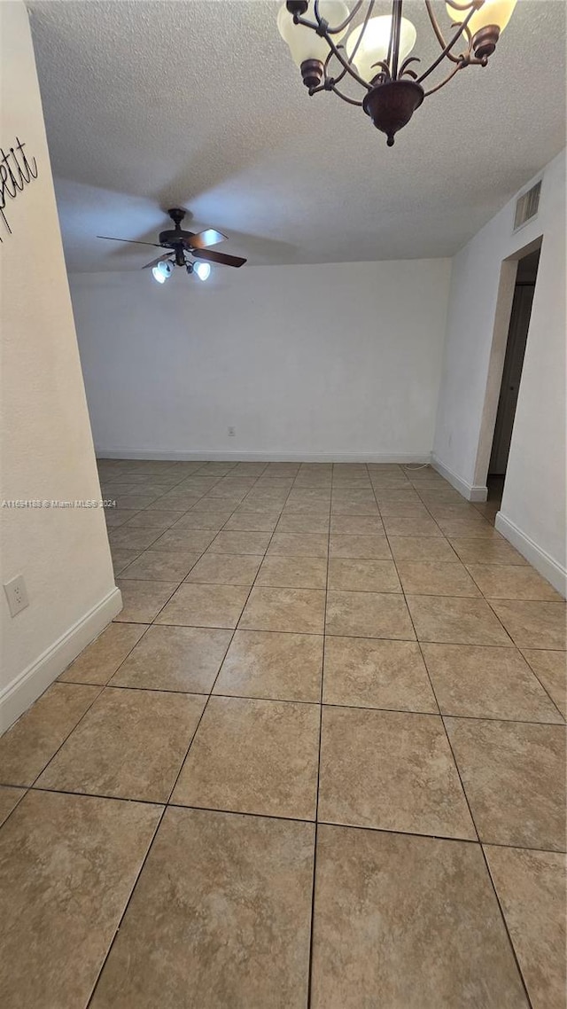 empty room featuring ceiling fan with notable chandelier, a textured ceiling, and light tile patterned flooring