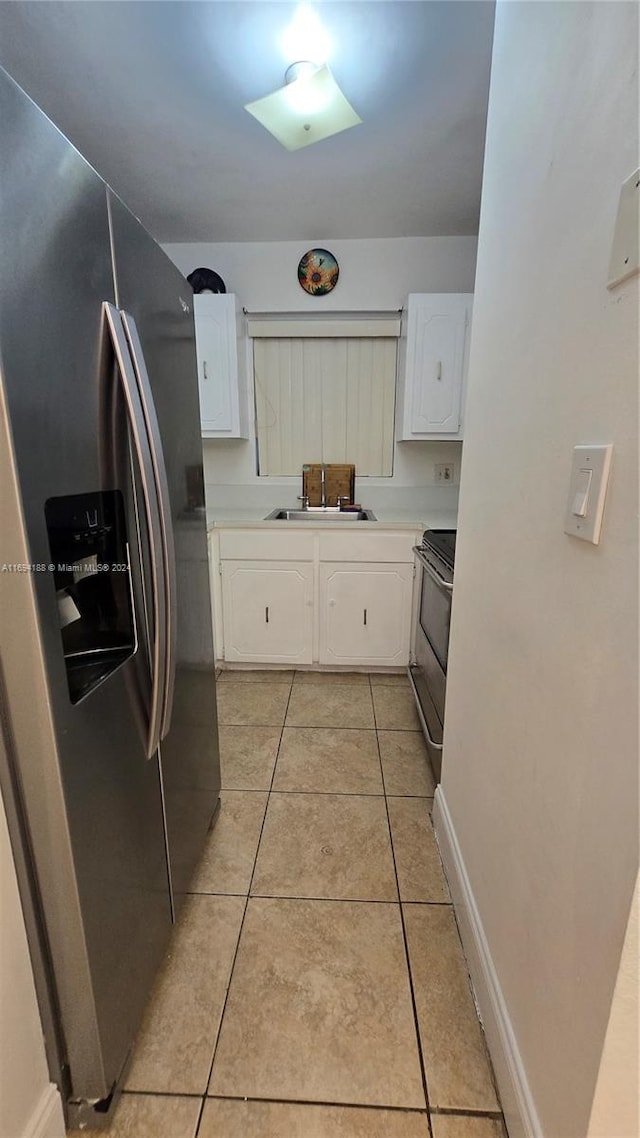 kitchen with appliances with stainless steel finishes, light tile patterned floors, white cabinetry, and sink