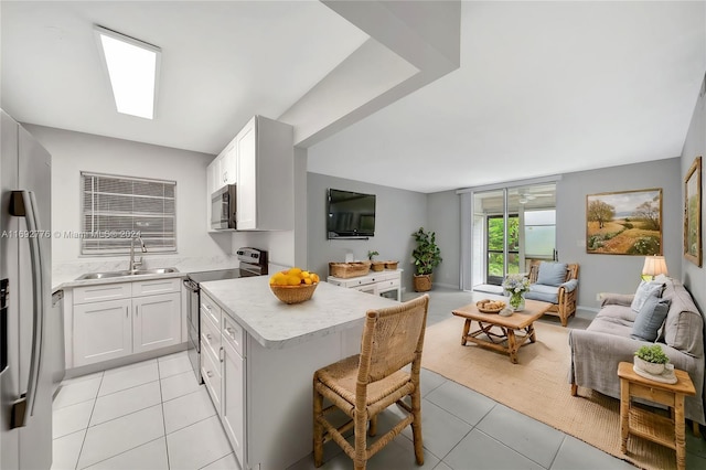 kitchen with sink, kitchen peninsula, a breakfast bar area, white cabinetry, and stainless steel appliances