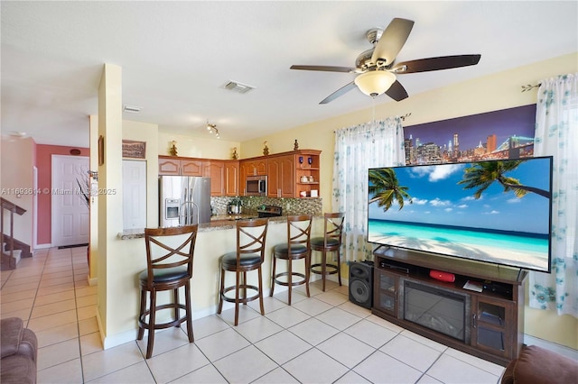 kitchen featuring a breakfast bar area, decorative backsplash, light tile patterned floors, kitchen peninsula, and stainless steel appliances