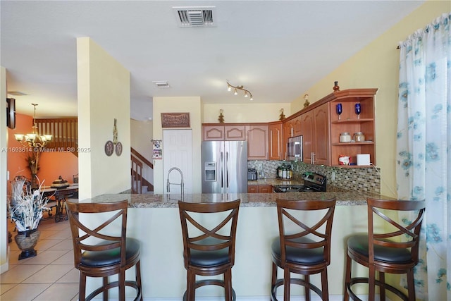 kitchen featuring kitchen peninsula, a kitchen bar, backsplash, stainless steel appliances, and a notable chandelier