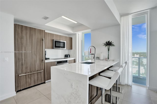 kitchen with stainless steel microwave, a kitchen breakfast bar, sink, light stone countertops, and light tile patterned floors