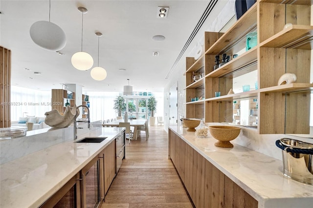 kitchen featuring light stone countertops, pendant lighting, light hardwood / wood-style floors, and sink