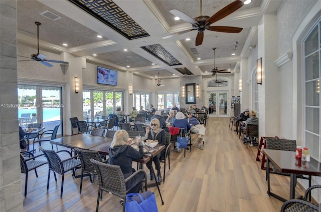 dining space featuring french doors, coffered ceiling, light wood-type flooring, ornamental molding, and a high ceiling