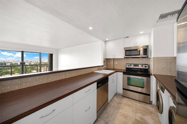 kitchen featuring white cabinets, sink, appliances with stainless steel finishes, tasteful backsplash, and washer / clothes dryer