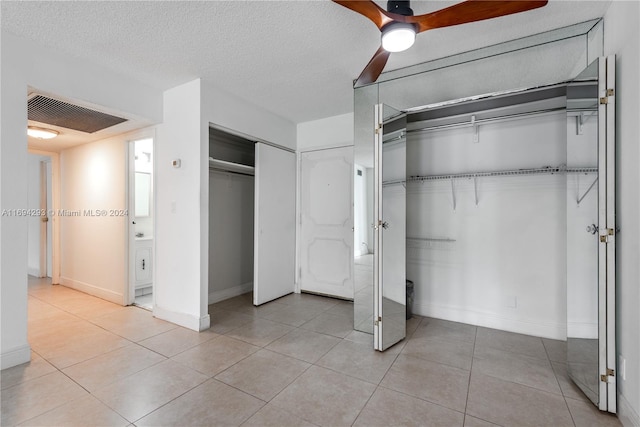 unfurnished bedroom with light tile patterned floors, a textured ceiling, two closets, and ceiling fan