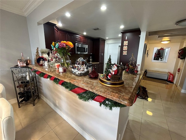 kitchen with kitchen peninsula, a kitchen bar, light stone counters, crown molding, and light tile patterned floors