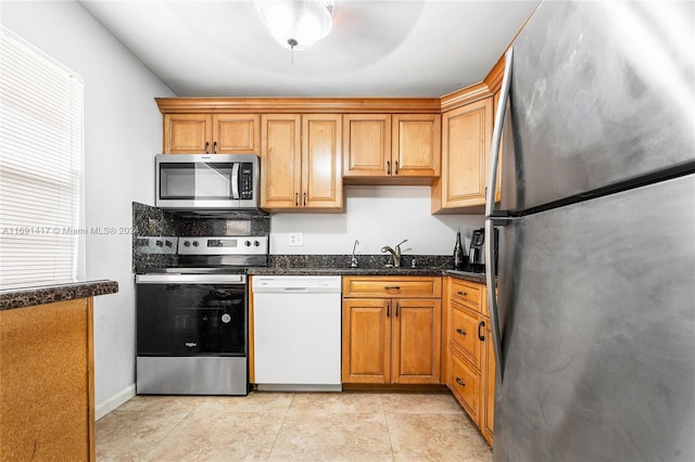 kitchen with light tile patterned floors, stainless steel appliances, dark stone countertops, and sink