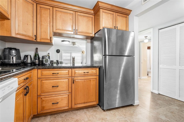 kitchen featuring stainless steel refrigerator, white dishwasher, dark stone counters, and light tile patterned floors