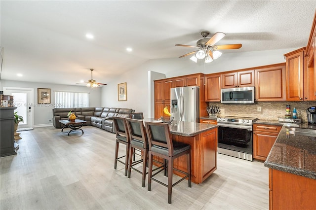 kitchen featuring decorative backsplash, appliances with stainless steel finishes, light wood-type flooring, a center island, and lofted ceiling