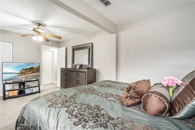 bedroom with light wood-type flooring, a textured ceiling, ceiling fan, and beamed ceiling