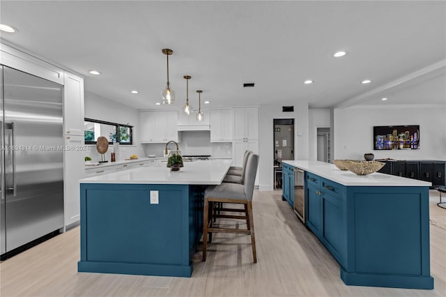 kitchen with white cabinetry, stainless steel built in refrigerator, hanging light fixtures, and a large island with sink