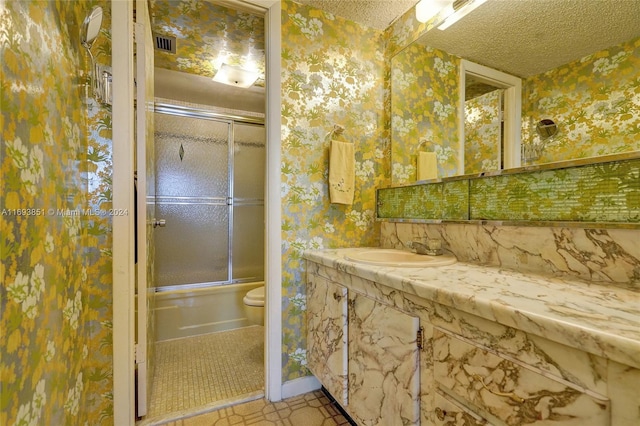 full bathroom with vanity, tile patterned floors, bath / shower combo with glass door, toilet, and a textured ceiling