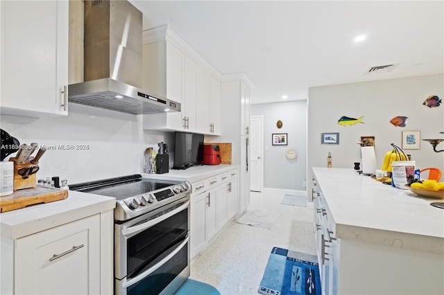 kitchen featuring white cabinets, wall chimney exhaust hood, and range with two ovens