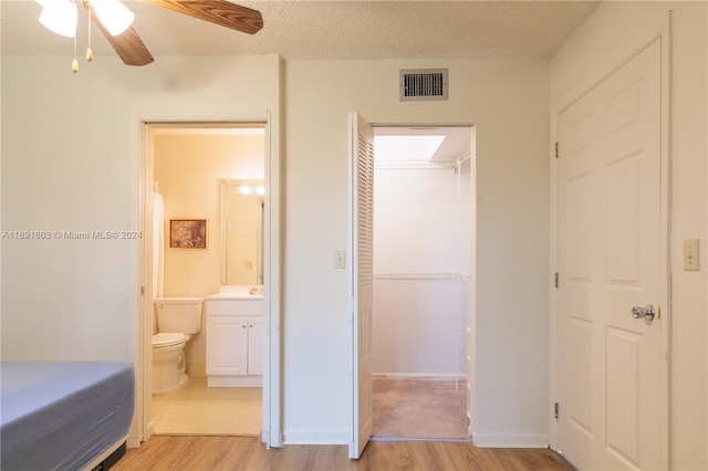 bedroom with ensuite bath, a textured ceiling, ceiling fan, light hardwood / wood-style flooring, and a closet