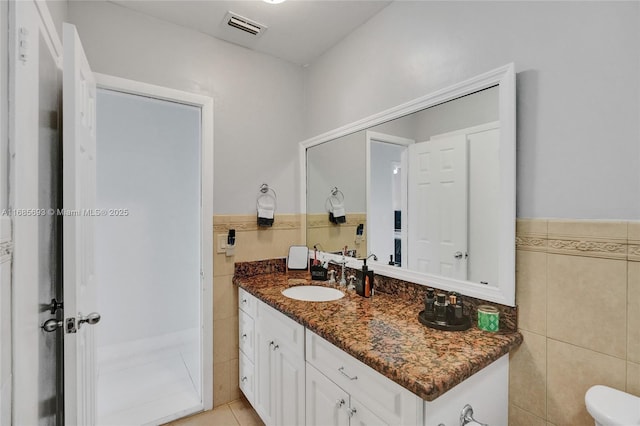 bathroom featuring vanity, toilet, tile patterned flooring, and tile walls