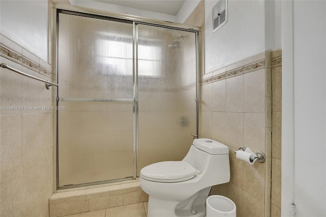 bathroom featuring tile patterned flooring, toilet, tile walls, and a shower with shower door