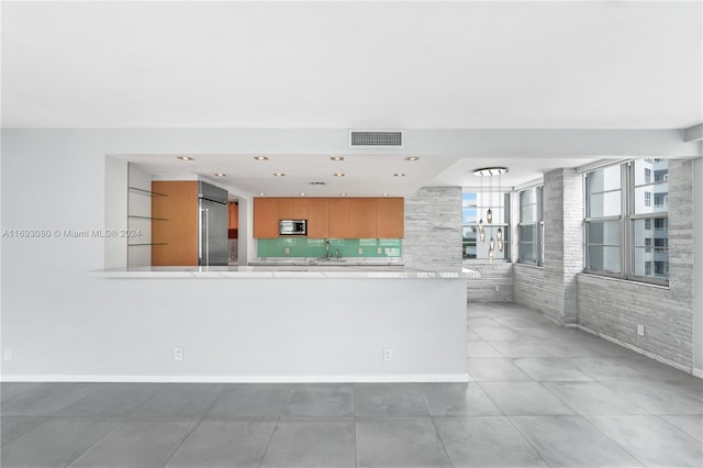 kitchen featuring kitchen peninsula, appliances with stainless steel finishes, brick wall, sink, and light tile patterned floors