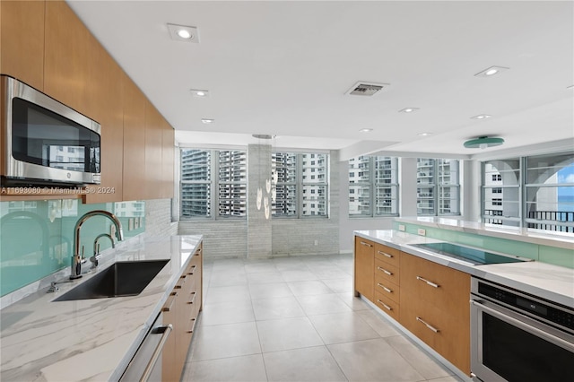 kitchen with light tile patterned flooring, appliances with stainless steel finishes, light stone countertops, and sink