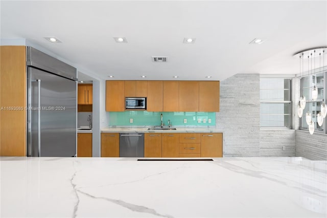 kitchen with built in appliances, backsplash, light stone counters, and sink