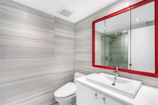 bathroom featuring a shower with door, vanity, tile walls, and toilet