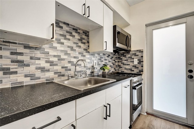 kitchen with light wood-type flooring, backsplash, stainless steel appliances, sink, and white cabinets