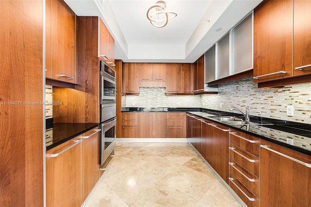 kitchen with decorative backsplash, double oven, dark stone countertops, and sink