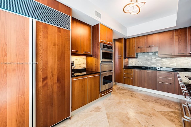 kitchen featuring a raised ceiling, paneled refrigerator, double oven, and tasteful backsplash