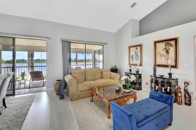 living room featuring high vaulted ceiling, a water view, light hardwood / wood-style flooring, and plenty of natural light