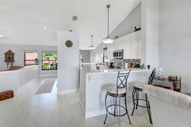 kitchen featuring kitchen peninsula, a kitchen bar, pendant lighting, white cabinets, and light hardwood / wood-style floors