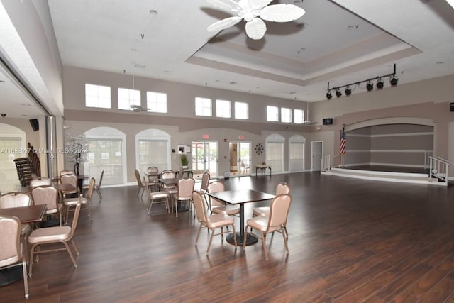 dining area with a high ceiling, dark hardwood / wood-style floors, ceiling fan, and a tray ceiling