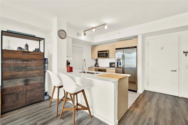 kitchen with sink, light hardwood / wood-style flooring, appliances with stainless steel finishes, kitchen peninsula, and a breakfast bar area