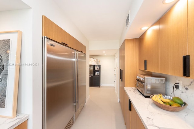 kitchen with decorative backsplash, high end fridge, and light stone counters