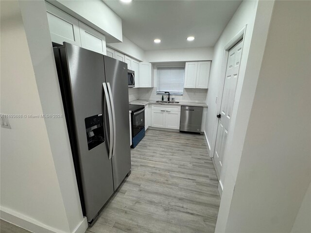 kitchen with tasteful backsplash, stainless steel appliances, sink, white cabinets, and light hardwood / wood-style floors