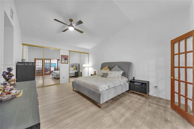 bedroom featuring multiple closets, ceiling fan, light hardwood / wood-style floors, and vaulted ceiling