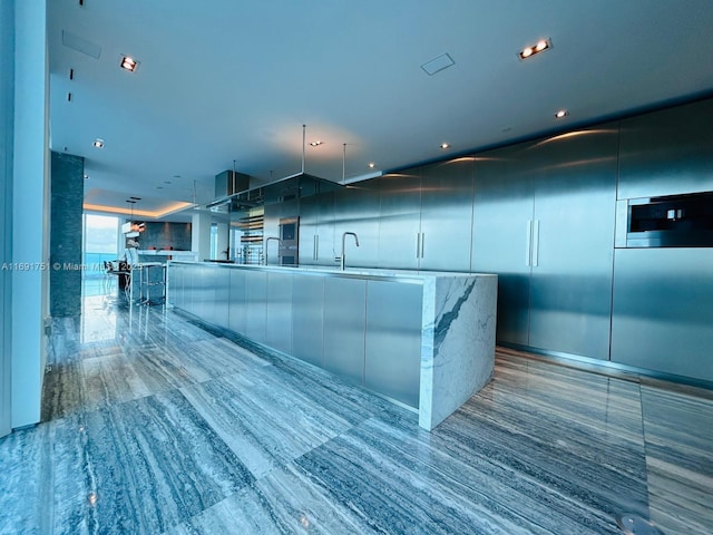 kitchen featuring a large island with sink, light stone countertops, pendant lighting, and sink