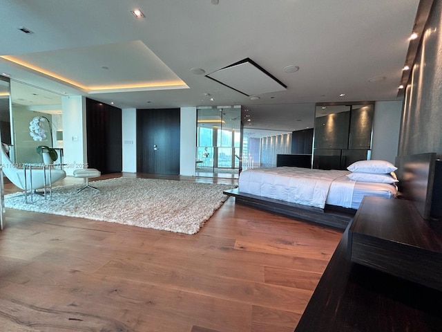 bedroom featuring a raised ceiling, expansive windows, and hardwood / wood-style floors