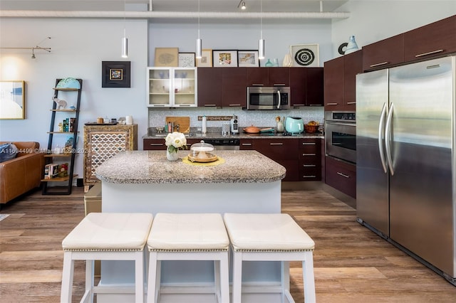 kitchen featuring backsplash, hanging light fixtures, light wood-type flooring, appliances with stainless steel finishes, and a breakfast bar area