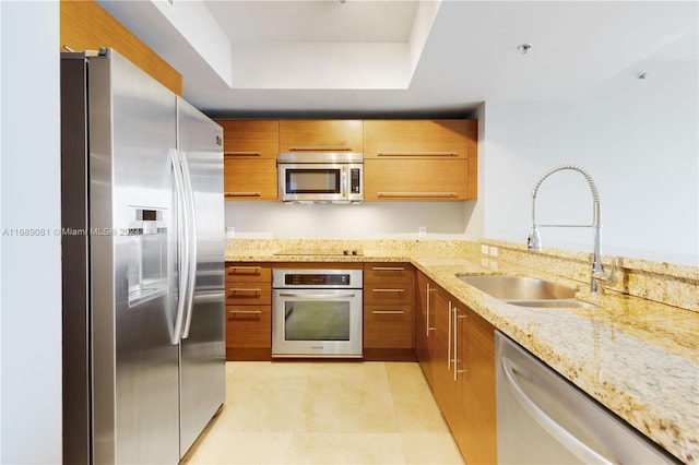 kitchen with a raised ceiling, sink, light tile patterned floors, light stone counters, and stainless steel appliances